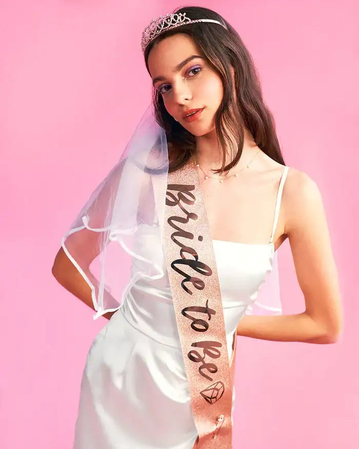 Une écharpe en or rose avec « future mariée » en lettrage cursive noir et une icône de diamant, portée en bandoulière sur la poitrine.